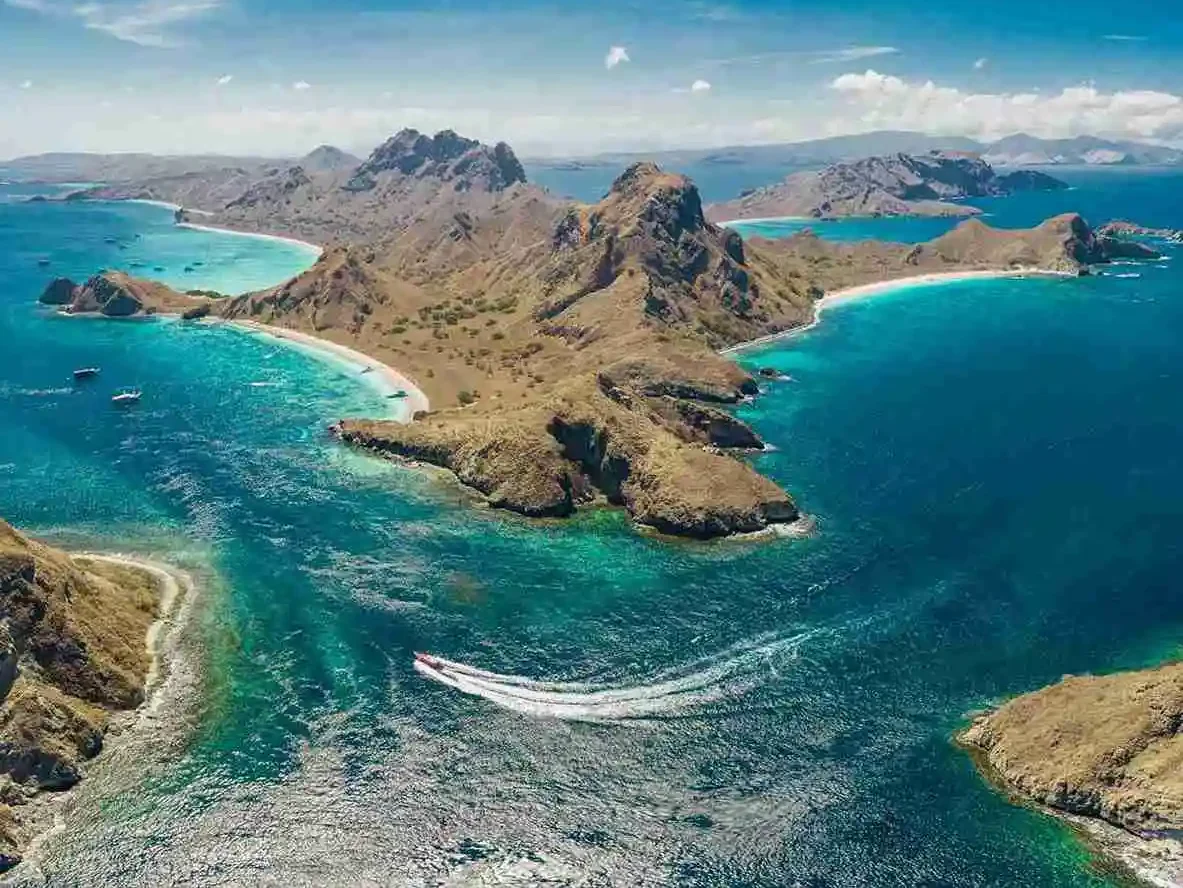 Aerial view of Padar Island&rsquo;s headlands and turquoise water with a speedboat&rsquo;s wake crossing the bay