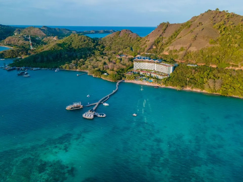 Aerial view of a hillside resort above a turquoise bay with its own jetty