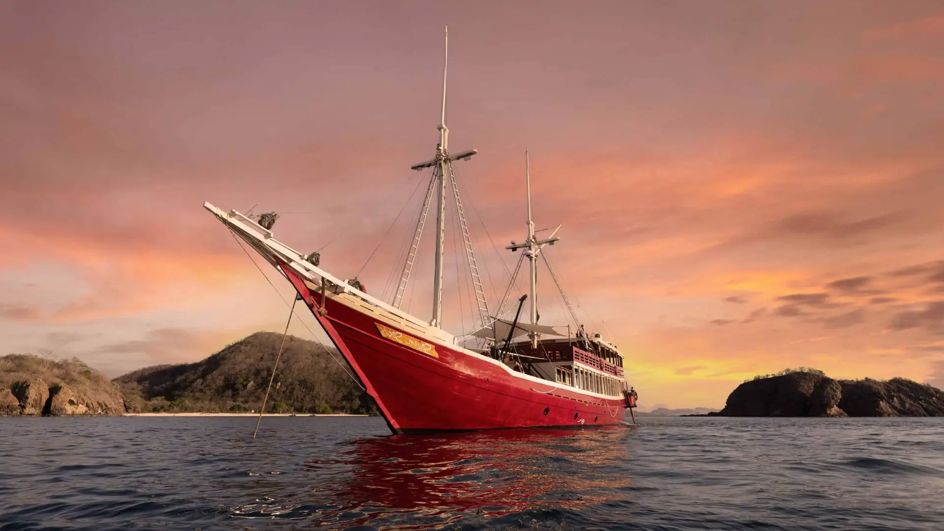 Seven Seas Liveaboard at anchor at sunset, red-hulled two-mast schooner | Komodo Luxury